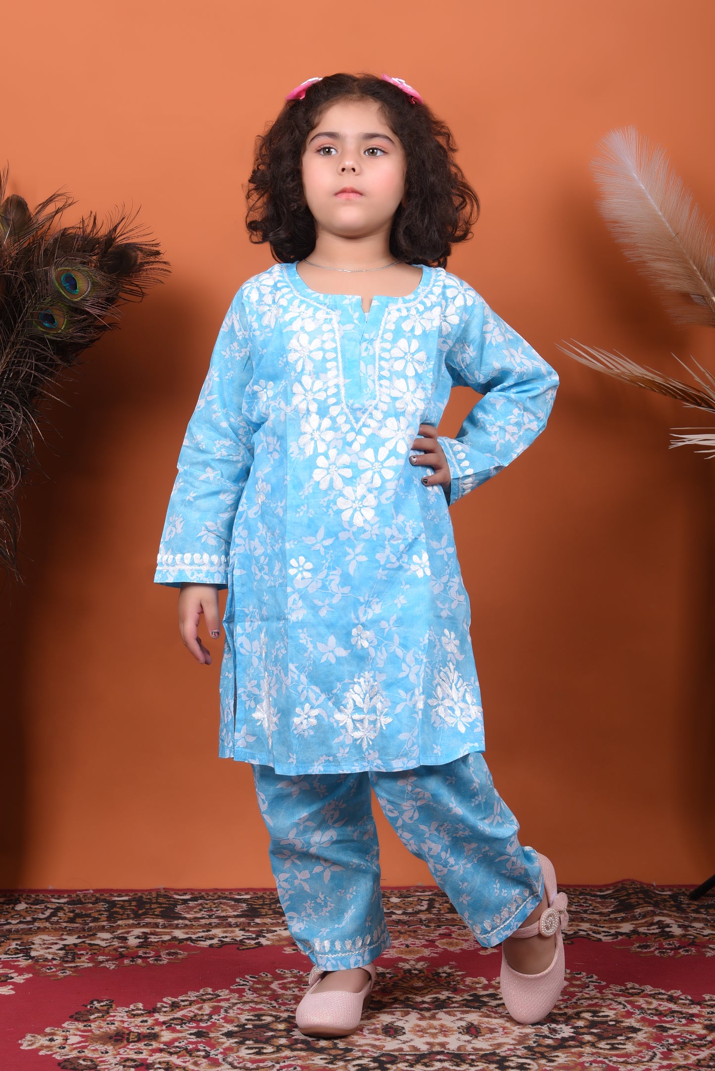 Young girl wearing a blue floral outfit against an orange background