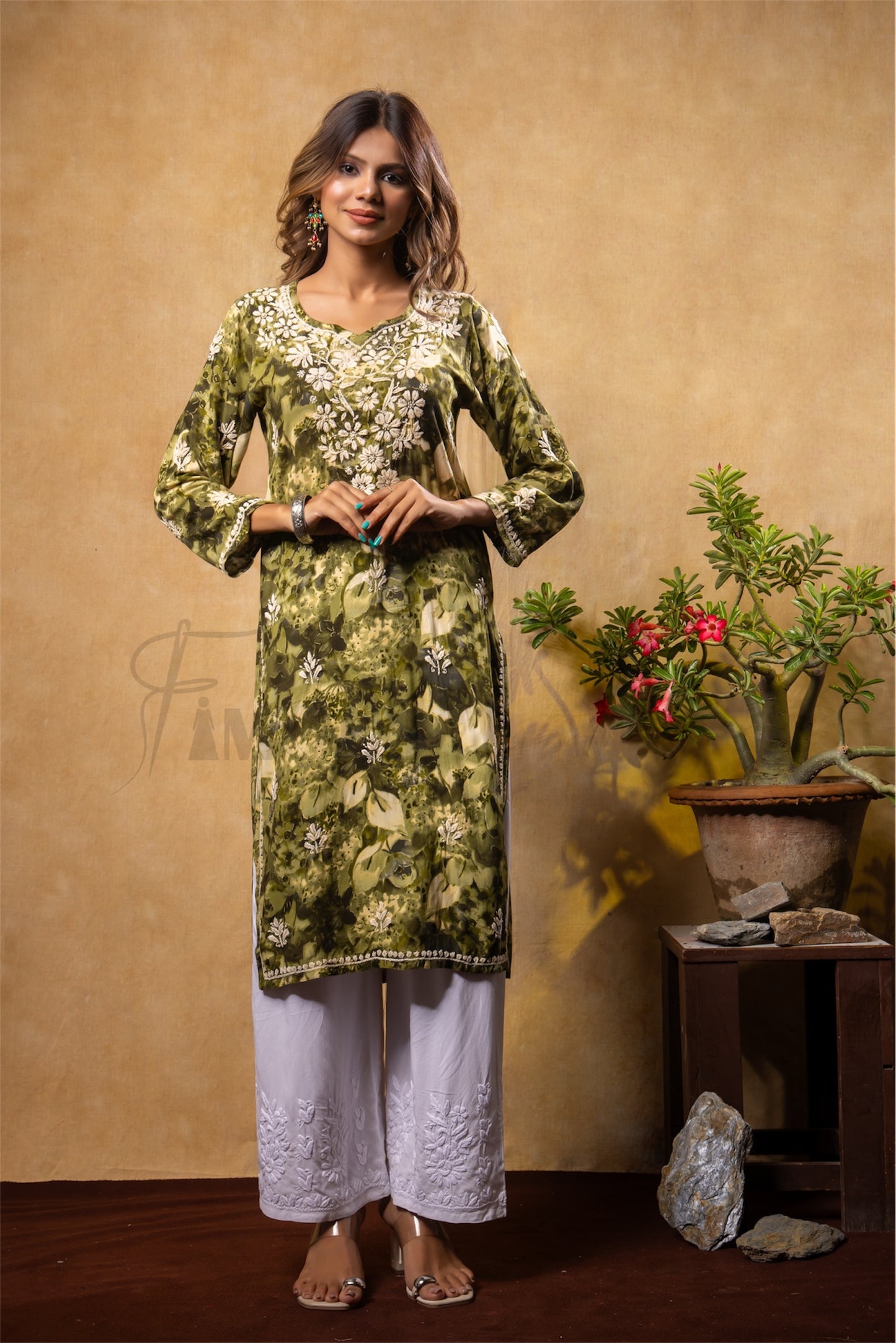 Woman wearing a green floral kurta with white pants against a beige wall.