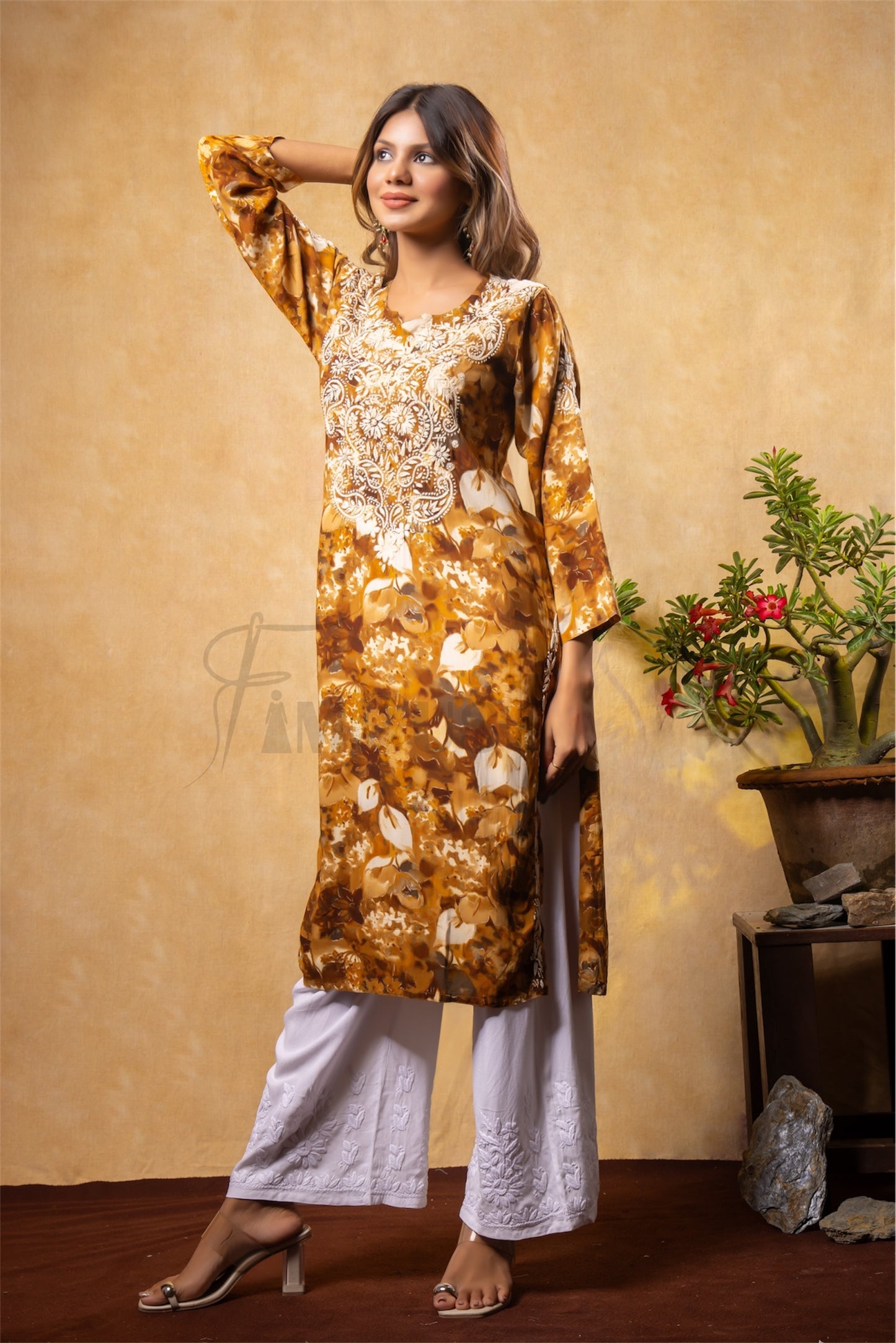 Woman wearing a gold and white patterned kurta with white pants against a beige wall.