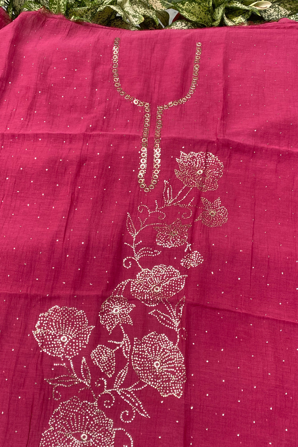 A close-up of a magenta pink fabric, likely a saree pallu or dupatta, featuring metallic gold floral embroidery and sequin work on a dotted background.