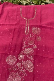 A close-up of a magenta pink fabric, likely a saree pallu or dupatta, featuring metallic gold floral embroidery and sequin work on a dotted background.