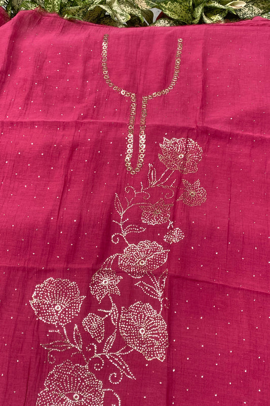 A close-up of a magenta pink fabric, likely a saree pallu or dupatta, featuring metallic gold floral embroidery and sequin work on a dotted background.