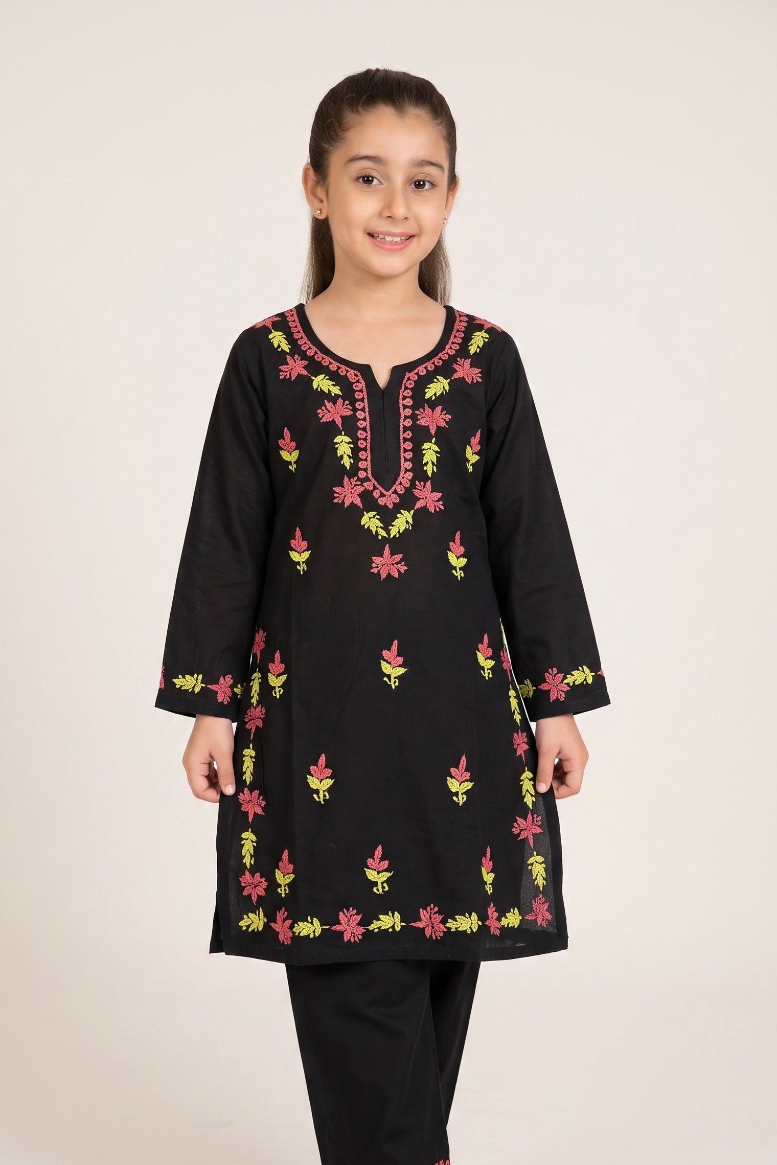 A young girl modeling a black long-sleeve kurta with colorful floral embroidery in pink, yellow, and green, paired with black pants, against a plain light background.