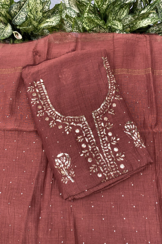 A rust-brown salwar suit set featuring a printed kurta with white floral embroidery and a matching printed dupatta, styled with green leaves at the top.