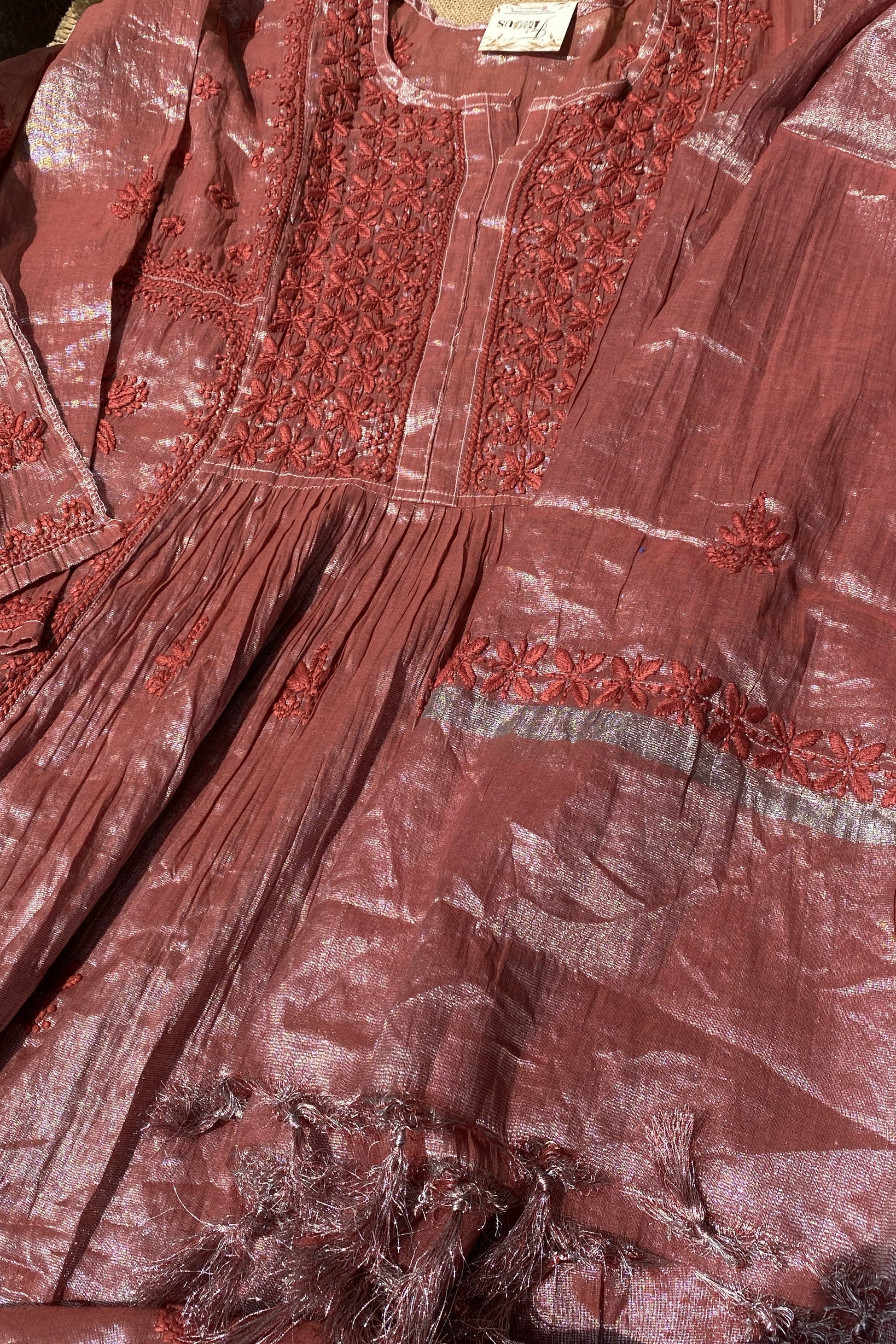 A close-up of a dusty rose pink traditional tunic or kurta with intricate red floral embroidery on the chest and a matching embroidered band on the skirt.