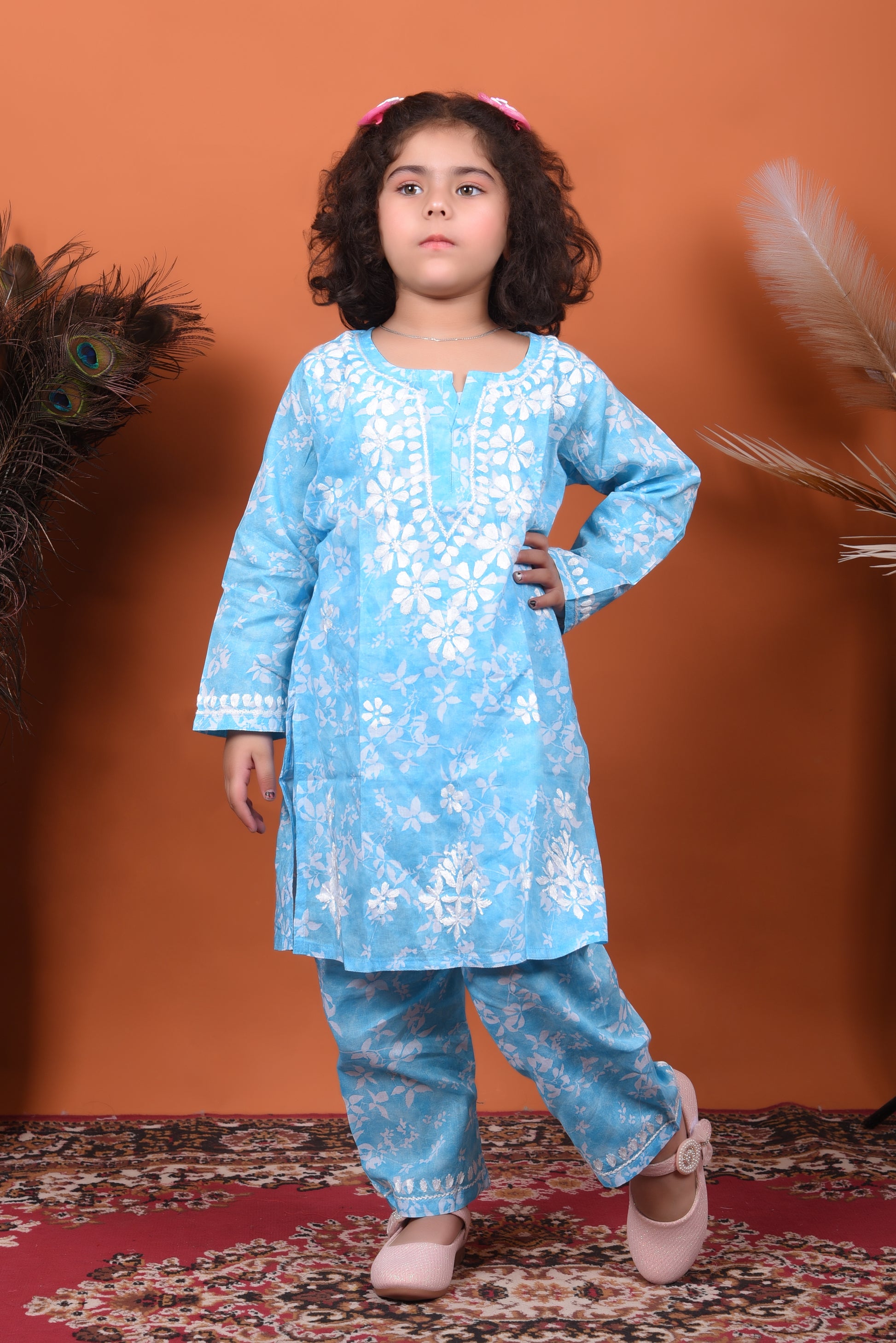 Young girl wearing a blue floral outfit against an orange background