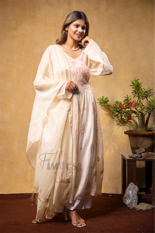 Woman in a white traditional outfit with floral patterns against a beige wall.