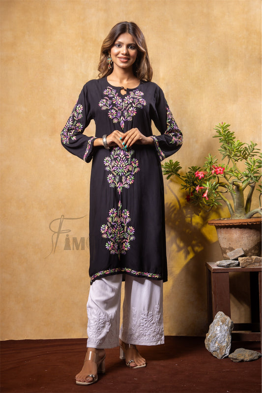 Woman wearing a black embroidered kurta with white pants against a beige wall.