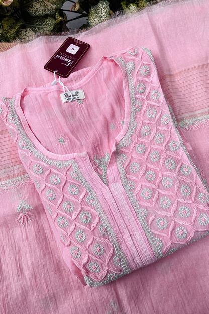 A folded light pink embroidered kurta laid flat on a matching pink fabric background. The kurta has a round neckline, a split V-neckline, and detailed geometric and floral embroidery in pink and light green around the neckline and front panel.