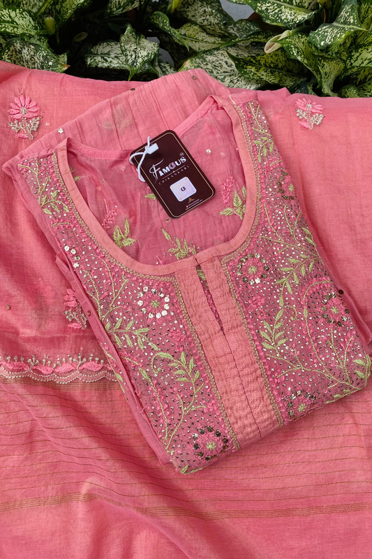 A pink embroidered traditional outfit laid flat, featuring a sheer pink kurta with ornate floral embroidery and mirror work on the front, paired with a matching pink fabric base. A dark brown brand tag reading 'Fazl-e-Aroos' is attached near the neckline.