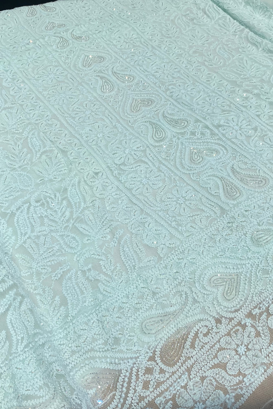 A close-up of pale mint green lace fabric with intricate floral and paisley embroidery, sequins, and beadwork.