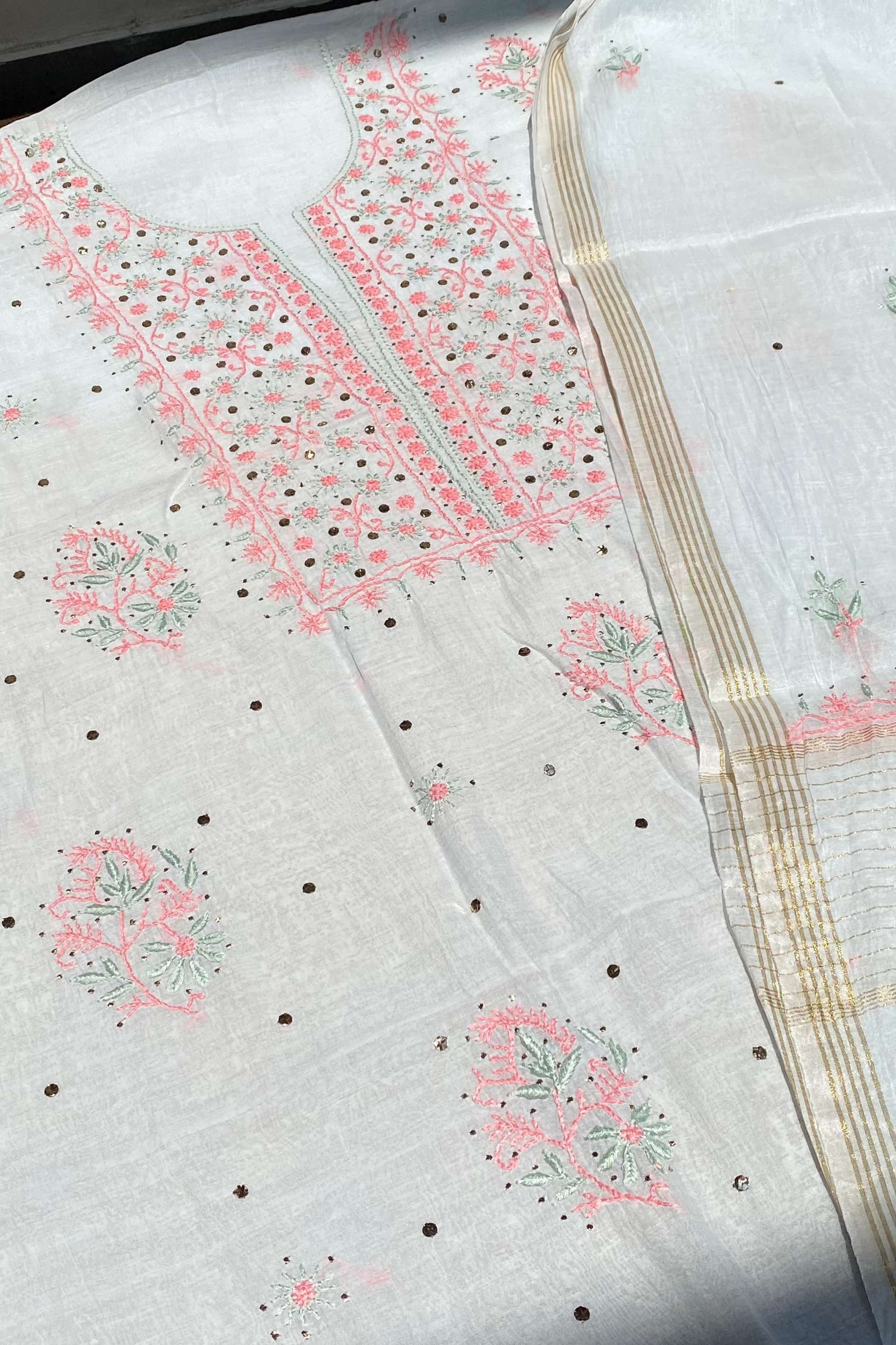 White fabric with pink and green embroidery on a light gray background