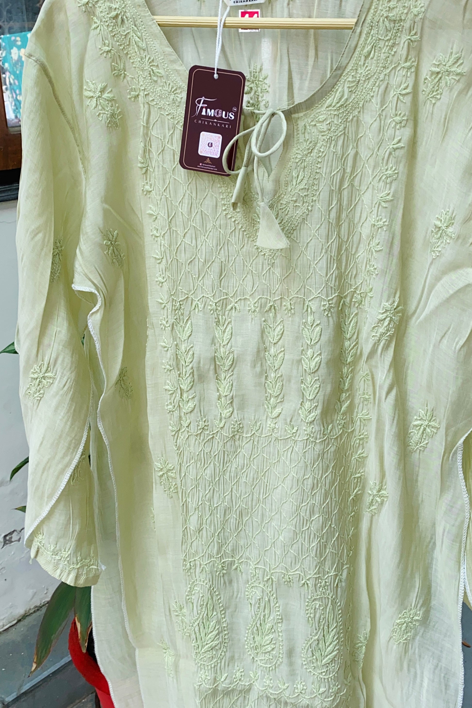 A pale yellow-green embroidered long-sleeve tunic top hanging on a wooden hanger with a visible brand tag reading 'Familiars'.