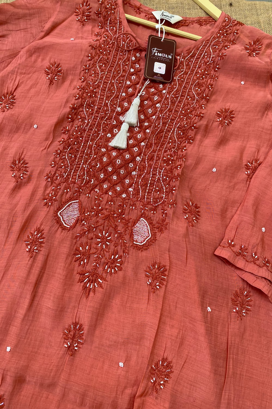 A terracotta pink embroidered kurta laid flat on a wooden hanger, featuring intricate floral embroidery, beadwork, and a white tassel detail on the neckline.